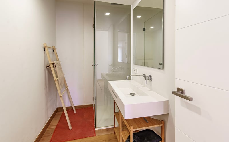 Modernt badrum med vitt tvättställ på träställning, duschvägg i glas och ljust trägolv.