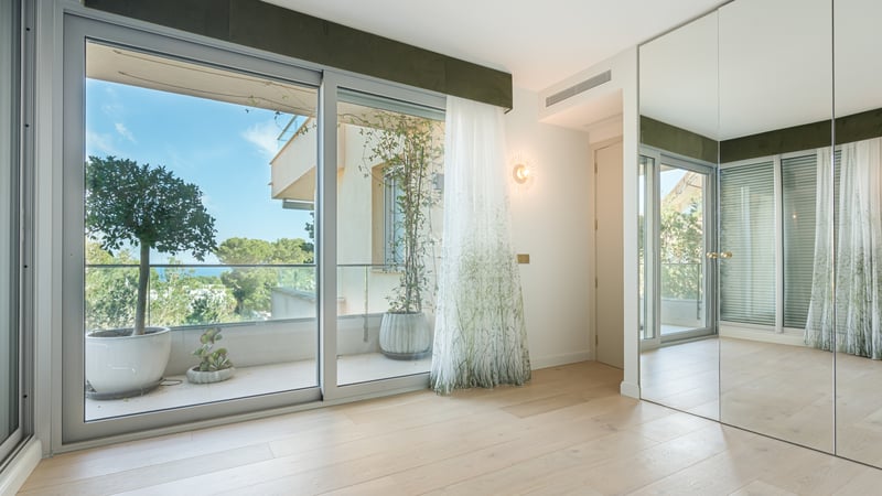 Bright bedroom with oak floors, mirrored wardrobes, and sliding glass doors opening to a terrace with garden views.