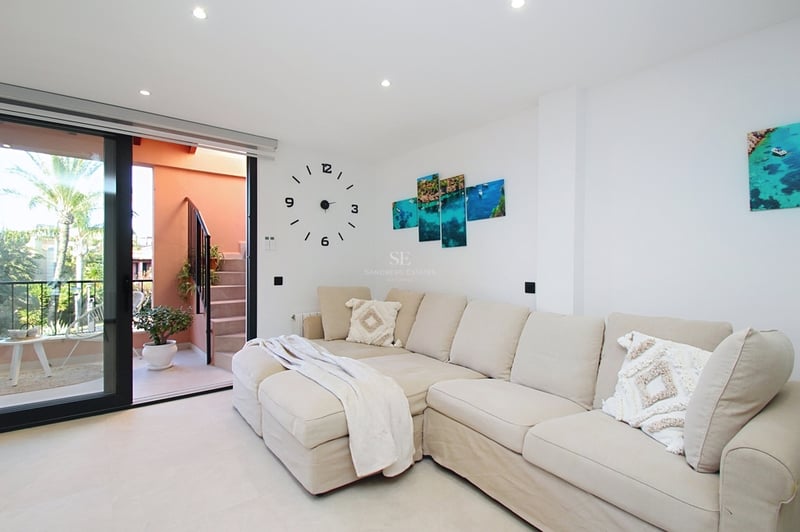 Ljust vardagsrum med en stor beige modulsoffa och skjutdörrar i glas som leder till en medelhavsterrass.