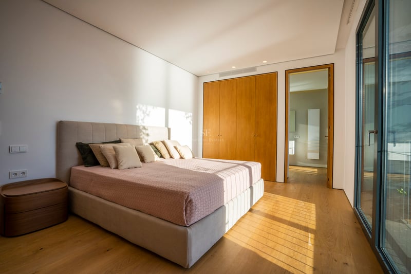 Modernes Schlafzimmer mit Eichenparkett, Einbauschränken, großem Bett und bodentiefen Glasfronten.