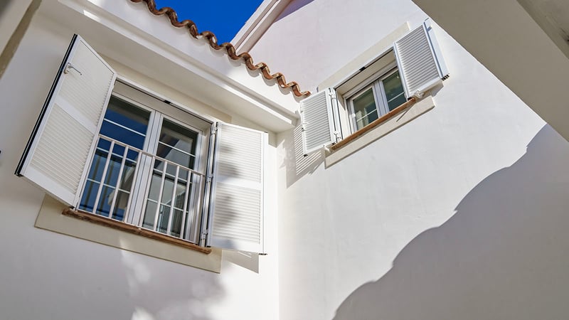 Detaljbild av vit fasad med mallorkinska fönsterluckor, terrakottatakpannor och fönsterbrädor i natursten.