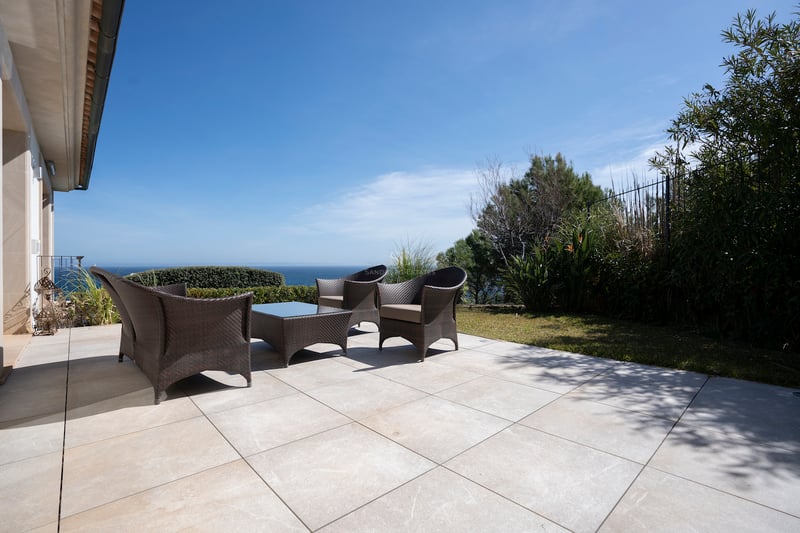 Große Steinterrasse mit dunklen Korbmöbeln und Blick auf das Meer unter klarem blauem Himmel.