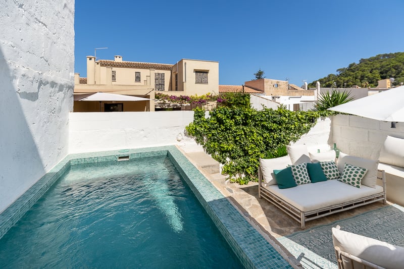 Piscine privée turquoise dans une cour avec murs blanchis à la chaux, sol en pierre et salon de jardin.
