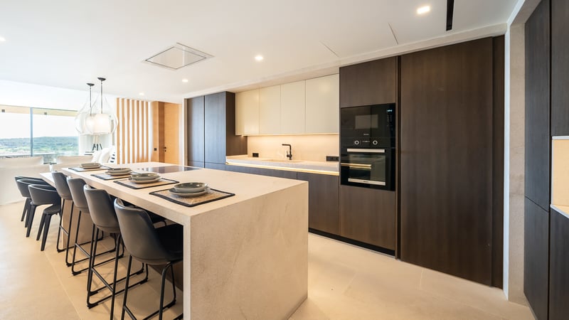 Cuisine moderne à aire ouverte avec un grand îlot en pierre, des armoires en bois sombre et des fours encastrés.