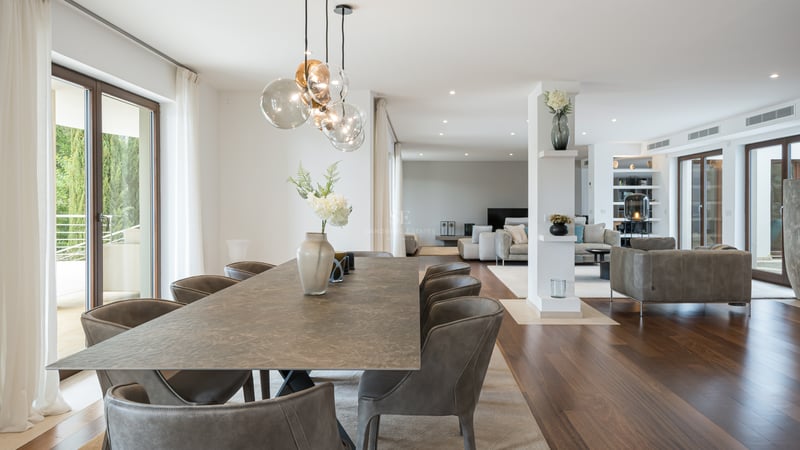 Grande table à manger en pierre avec chaises en cuir dans une pièce lumineuse avec parquet et baies vitrées.