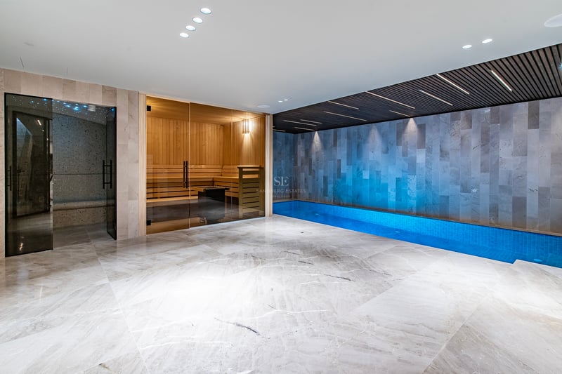 Espace spa intérieur moderne avec sol en marbre, sauna vitré et piscine intérieure avec éclairage d'ambiance.