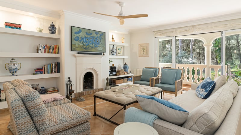 Bright living room featuring a white arched fireplace, built-in shelving, blue armchairs, and glass doors to a terrace.