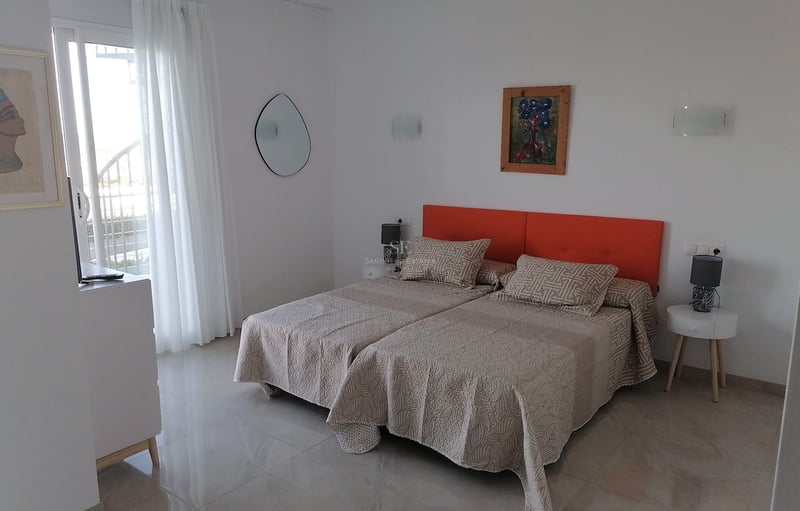 Chambre avec lits jumeaux, tête de lit orange, sol en pierre polie et accès direct au balcon.