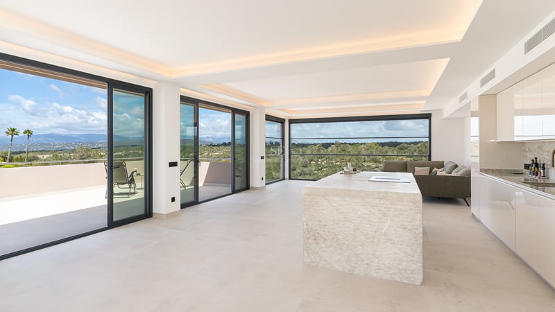 Heller Wohnraum mit monolithischer Steininsel, bodentiefen Glasfronten und Panoramablick auf die Berge.