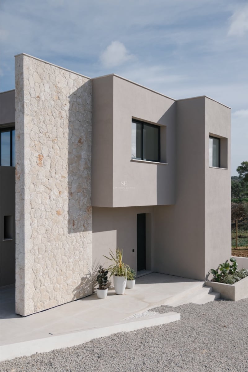 Außenansicht einer modernen Villa mit Natursteinwand, sandfarbenem Putz und anthrazitfarbenen Fensterrahmen.