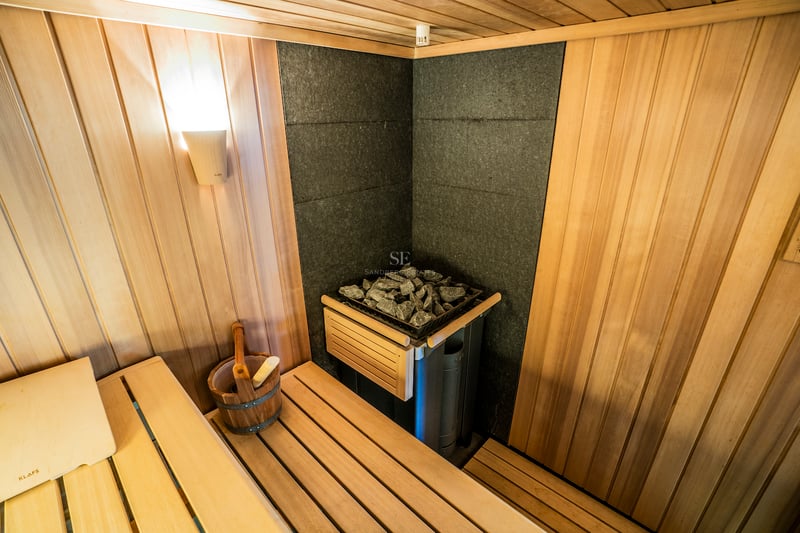 Innenansicht einer holzgetäfelten Sauna mit KLAFS-Steinofen, Holzeimer und stimmungsvoller Beleuchtung.