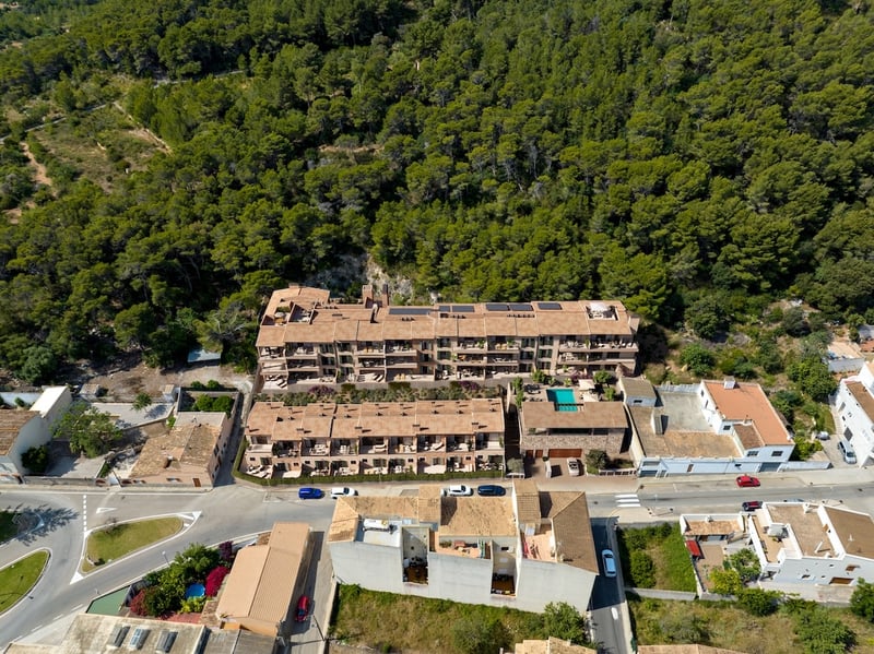 Bird's eye view of a multi-story terracotta-roofed apartment complex nestled against a lush green forest.