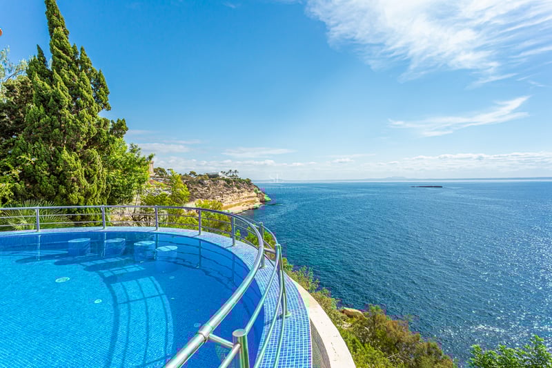 Grand balcon avec vue sur la mer, mobilier moderne, garde-corps en verre. Espace lumineux et élégant. Détails architecturaux design.