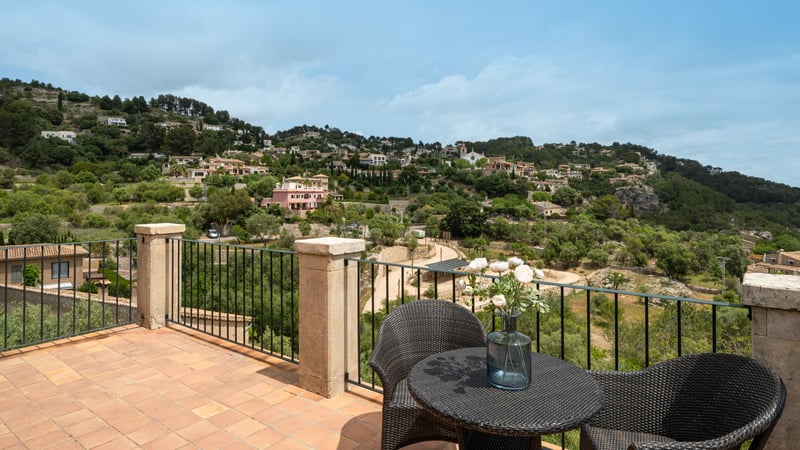 Terrasse en terre cuite avec mobilier en rotin et garde-corps en fer forgé surplombant un village méditerranéen.