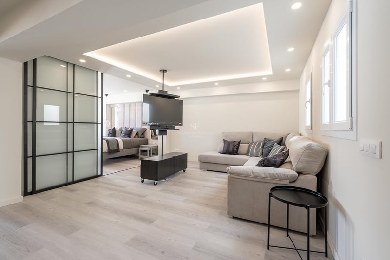 Zeitgenössisches Wohnzimmer mit grauem L-Sofa, drehbarer TV-Halterung und Glasschiebetüren zum Schlafzimmer.