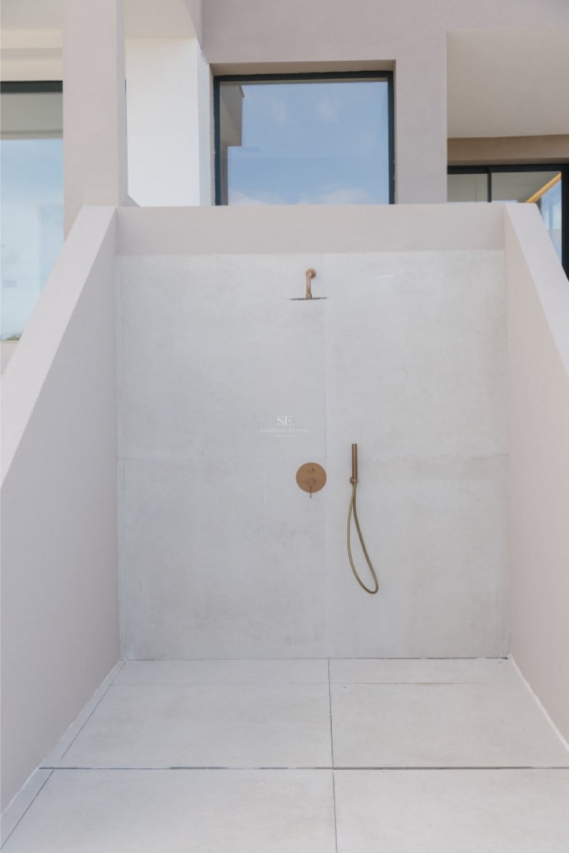 Minimalistische Außendusche mit gebürsteten Messingarmaturen vor hellbeige Steinwänden.