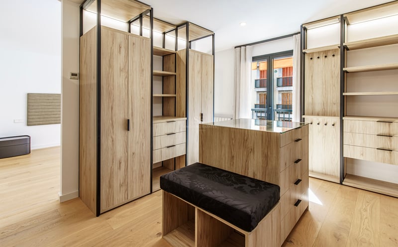 Grand dressing avec armoires en bois clair, îlot central avec plateau en verre et banc noir.