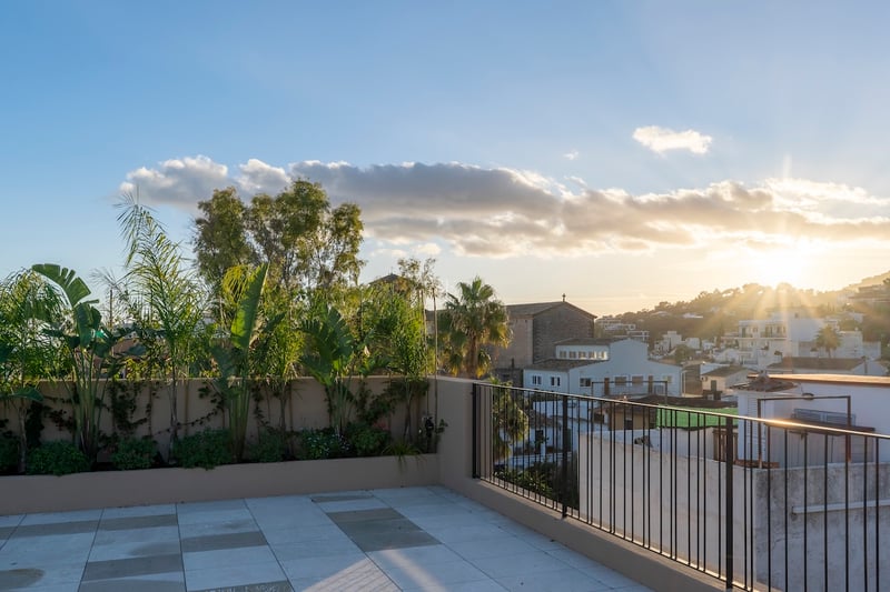 Terrasse de toit moderne avec carrelage en pierre et plantes tropicales, surplombant une ville méditerranéenne au coucher du soleil.