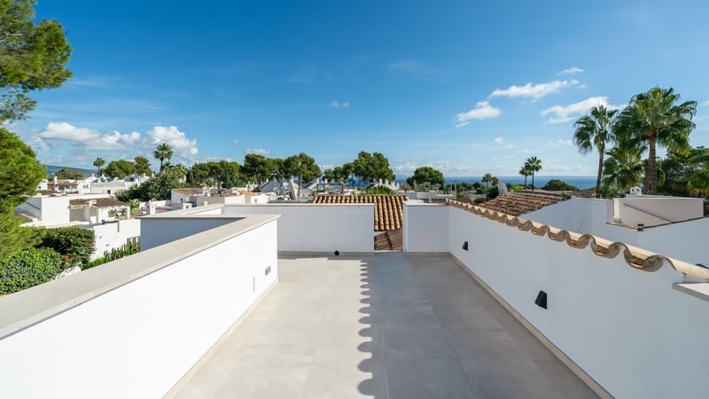 Spacious white rooftop with light stone tiling, offering panoramic views of palm trees, neighboring roofs, and the sea.