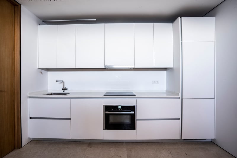 Weiße moderne Küche mit grifflosen Schränken, Einbaubackofen, Induktionskochfeld und Edelstahlspüle.