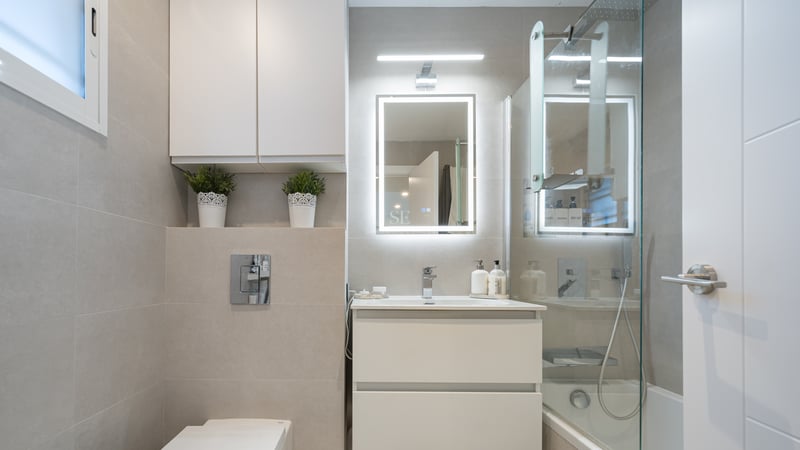 Modern bathroom with white vanity, backlit LED mirror, glass shower screen, and beige large-format tiles.