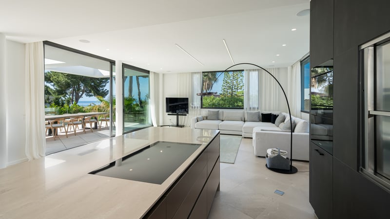 Salon contemporain et îlot de cuisine avec baies vitrées ouvrant sur une terrasse face à la Méditerranée.