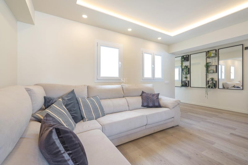 Modernes Wohnzimmer mit großem cremefarbenem L-Sofa, hellem Holzboden und LED-Deckenbeleuchtung.