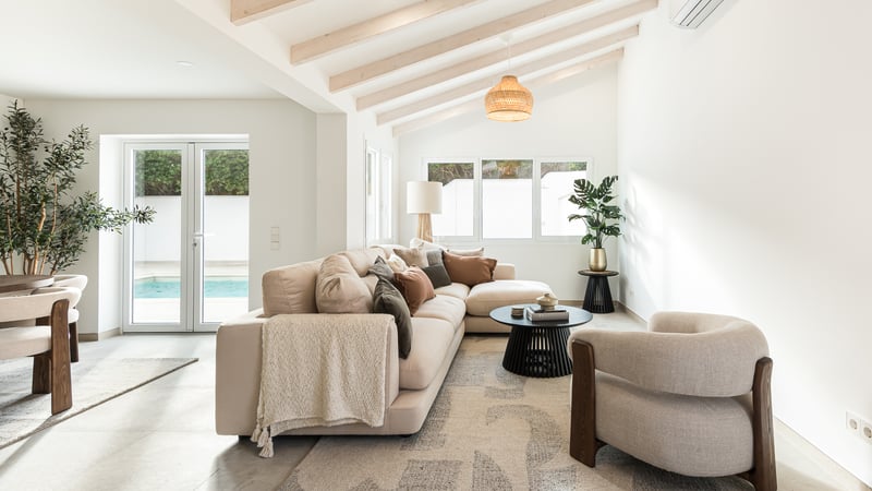 Bright living room with beige sectional sofa, wooden ceiling beams, and glass doors opening to a swimming pool.