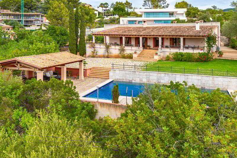 Exterior view of a Mediterranean-style villa with terracotta roof, swimming pool, and lush terraced gardens.
