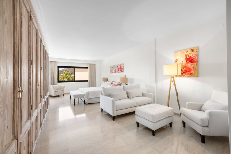 Suite lumineuse avec canapé blanc, armoires en bois, grand lit et art floral sur sol en marbre poli.