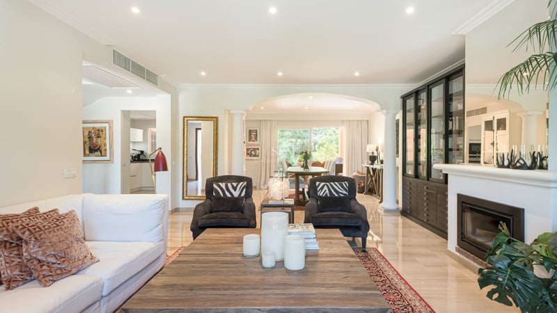 Bright open-plan living room featuring a marble floor, fireplace, and large windows leading to a lush garden terrace.