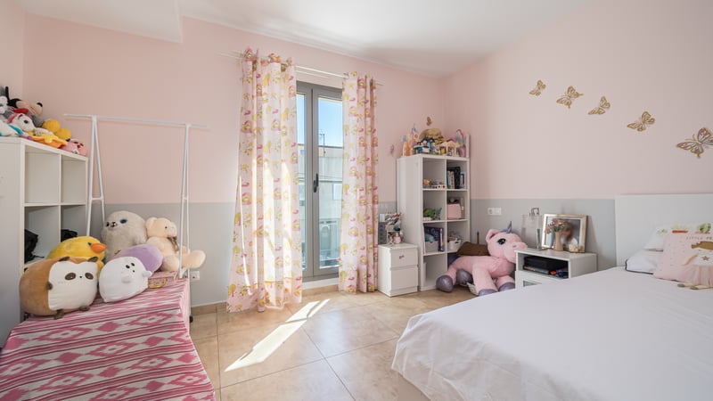 Rosa och grått barnrum med säng, gosedjur, hyllor och glasdörr ut till balkong.