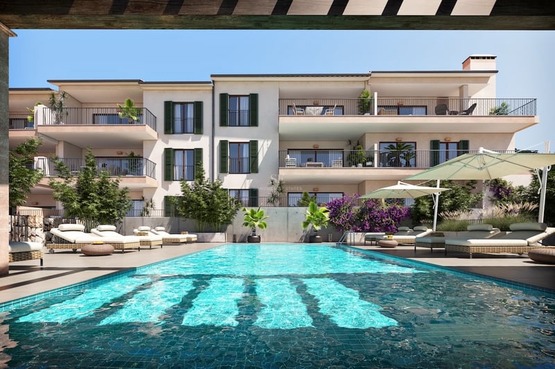 Large turquoise pool with sunbeds and umbrellas in front of a white building with balconies and green shutters.