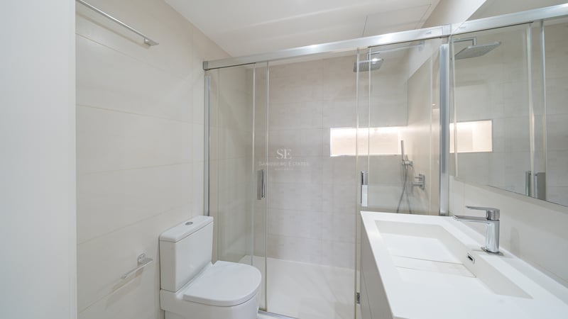 Ljust modernt badrum med en dusch i glas, vit toalett och minimalistiskt tvättställ.