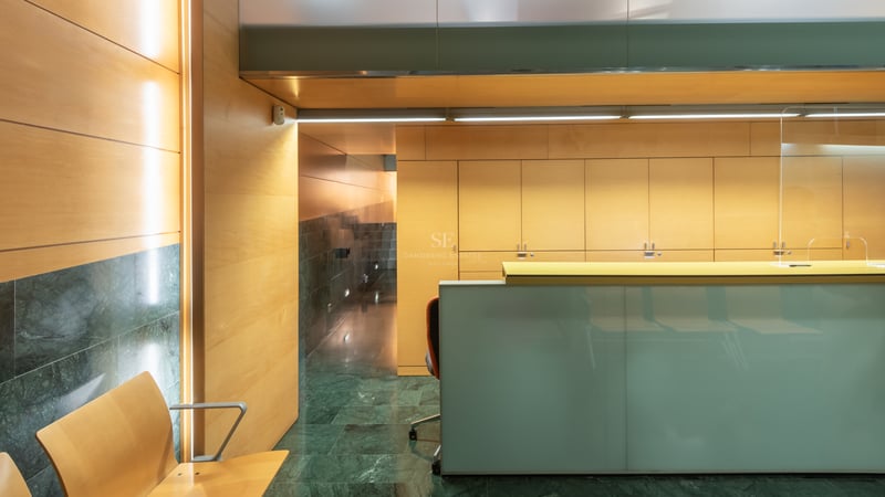 Bureau de réception moderne en verre dépoli, murs lambrissés en bois et sol en marbre vert foncé.