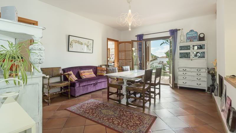 Dining room with terracotta floors, purple velvet sofa, and white wooden table opening to a sunny balcony.