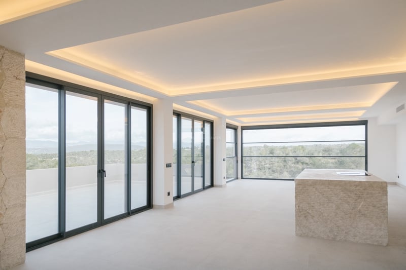 Moderner Küchenbereich mit einer massiven Kochinsel aus Naturstein und bodentiefen Fenstern mit Ausblick.