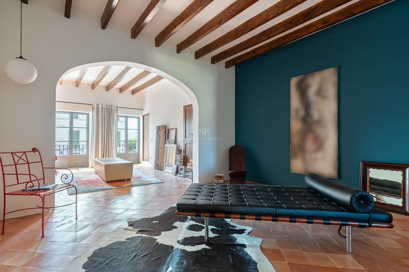 Salon intérieur avec carreaux de terre cuite, poutres apparentes, mur d'accent bleu canard et banquette en cuir noir.