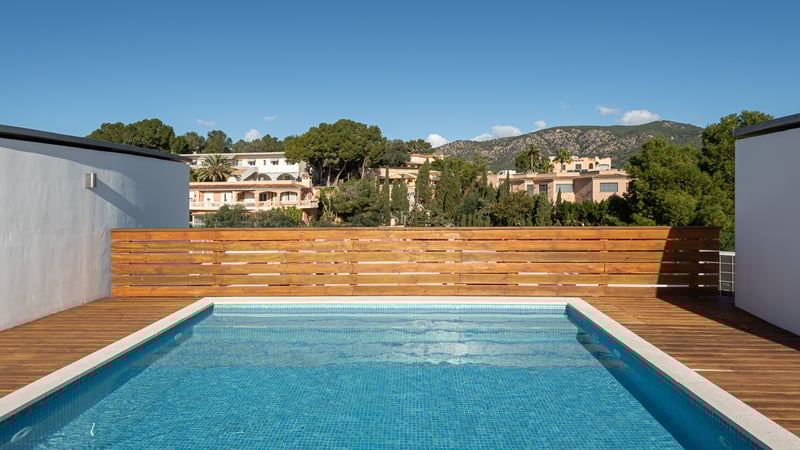 Une piscine rectangulaire sur le toit avec des carreaux bleus et une terrasse en bois, surplombant des collines vertes.