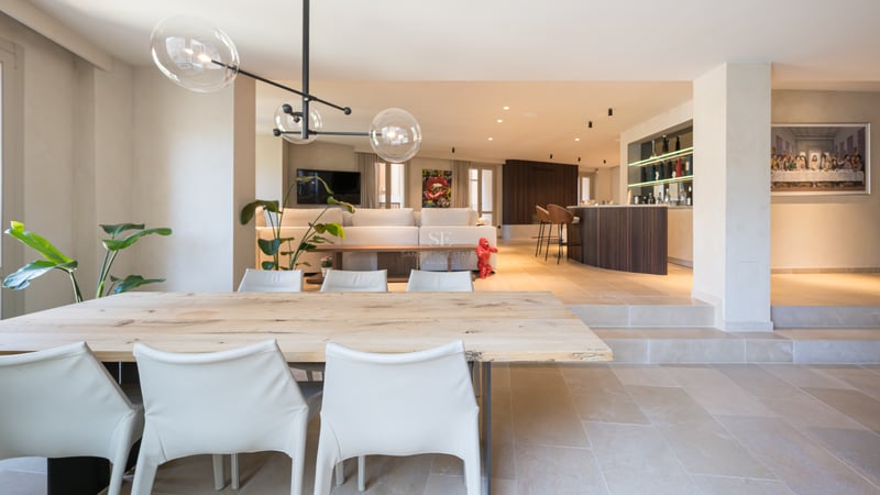 Table à manger en bois clair et chaises blanches dans un espace ouvert avec sol en pierre et luminaire design.