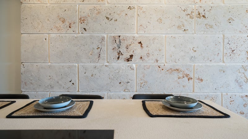 Gros plan d'un mur en blocs de travertin derrière une table avec des sets de table en fibres et bols en céramique.