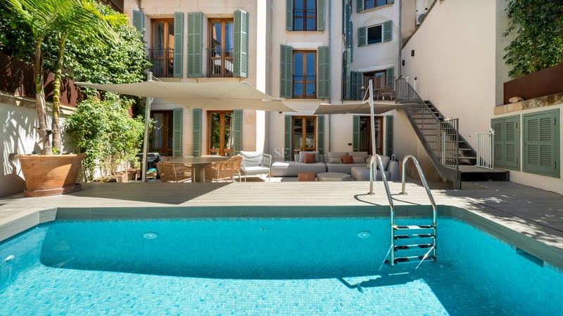 Piscine turquoise avec échelle devant une façade blanche aux volets verts et salon de jardin.