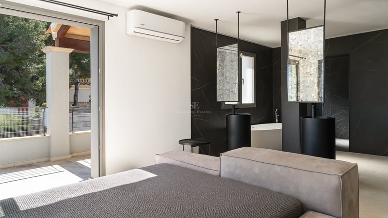 Lyxigt sovrum med öppet badrum i svart marmor, pelartvättställ och utgång till solig terrass.