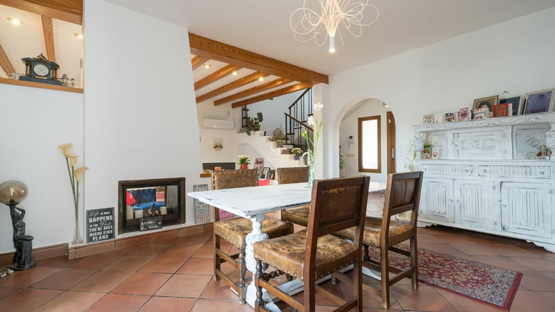Interior dining room with terracotta floors, exposed wooden beams, white distressed table, and leather chairs.