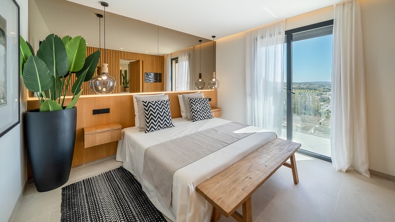 Chambre contemporaine avec tête de lit en chêne, mur miroir et grandes baies vitrées ouvrant sur le paysage.