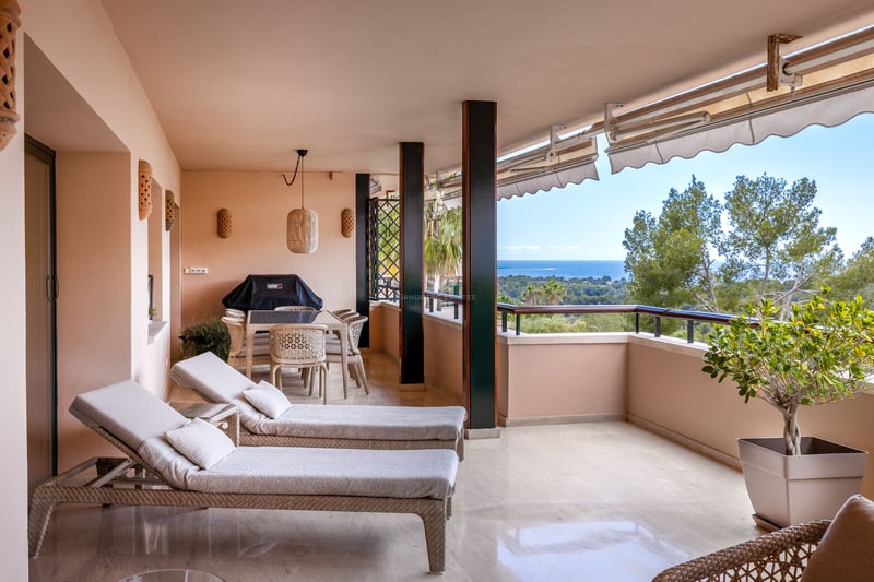 Terrasse couverte avec bains de soleil, salle à manger extérieure et vue sur la mer et la verdure.
