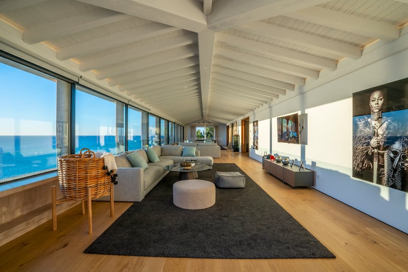 Zeitgenössisches Wohnzimmer mit weißen Holzbalkendecken, Eichenparkett und bodentiefen Fenstern mit Blick auf das Meer.