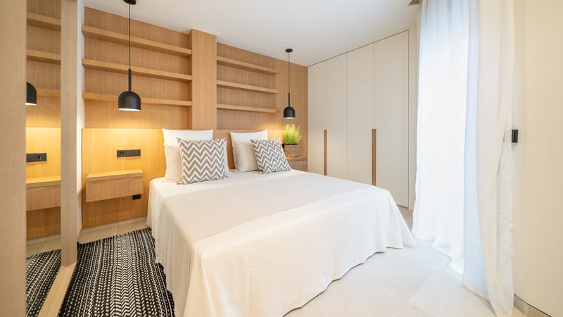 Chambre moderne avec tête de lit en chêne intégrée, étagères, literie blanche et armoires encastrées blanches.