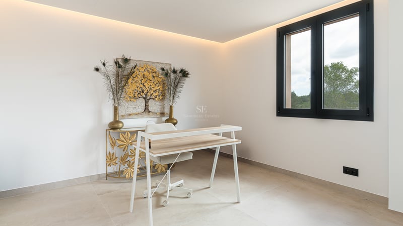 Ein moderner Arbeitsbereich mit weißem Schreibtisch, goldenem Kunstwerk und indirekter LED-Deckenbeleuchtung.