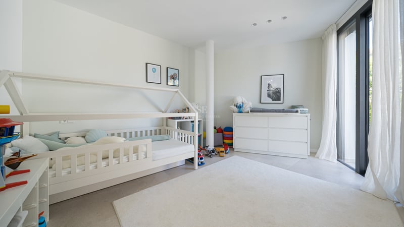 Chambre d'enfant moderne avec lit cabane blanc, commode et grandes baies vitrées avec voilages.